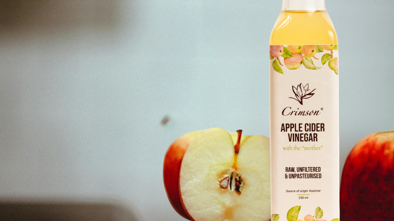 A bottle of Crimson Apple Cider Vinegar next to a halved red apple, emphasizing the product's natural ingredients.
