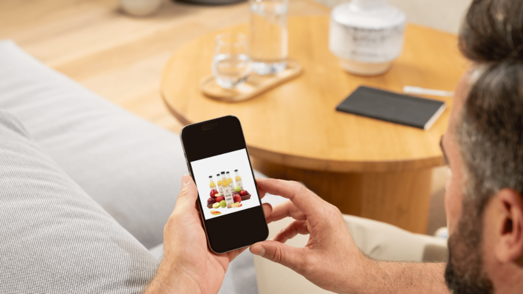 
A person sits on a couch, viewing a product image of Crimson Apple Cider Vinegar bottles and fresh fruit on their smartphone.